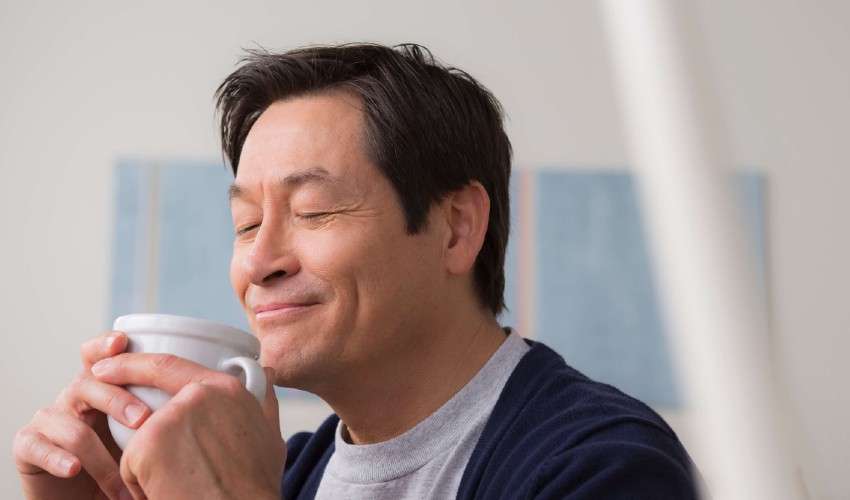 Man happily savouring the aroma as he cradles a coffee cup.