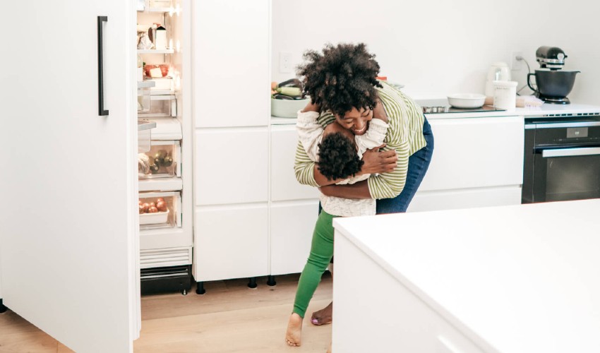 Mon hugging a toddler in front of an open fridge door.