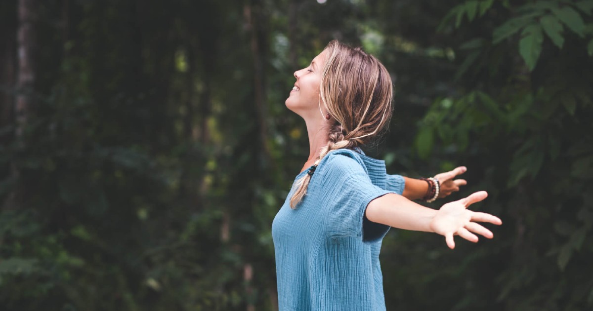 Smiling and peaceful woman standing with outstretched arms in the forest.