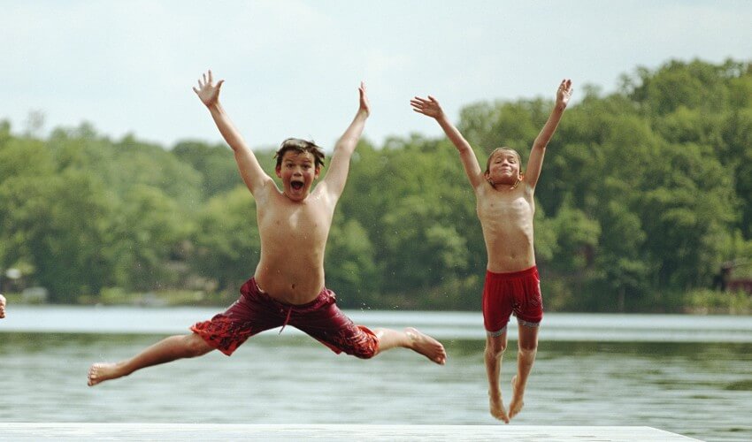 Two boys jumping off dock into lake.