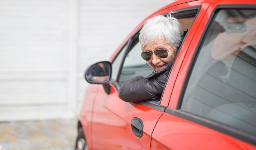 Senior female driver looking out window of red car