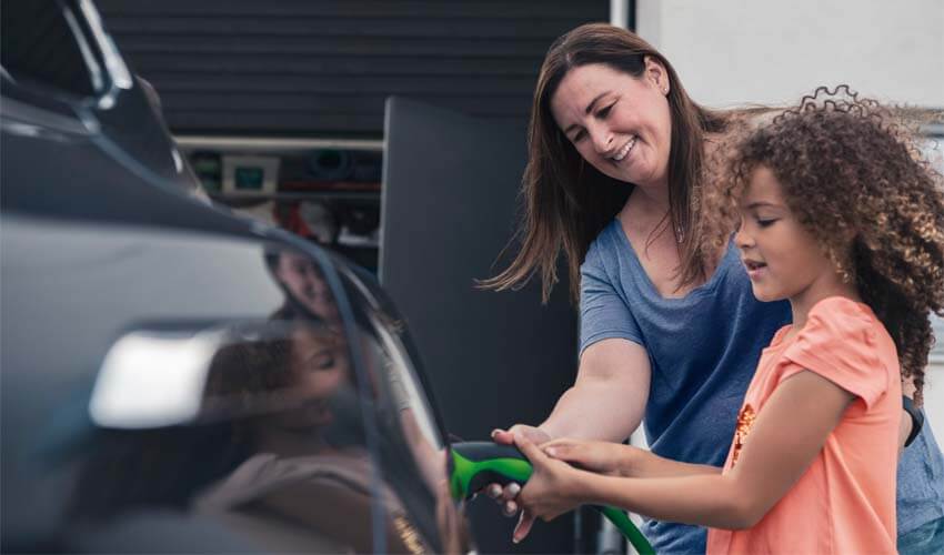 Mother and daughter plugging in electric car