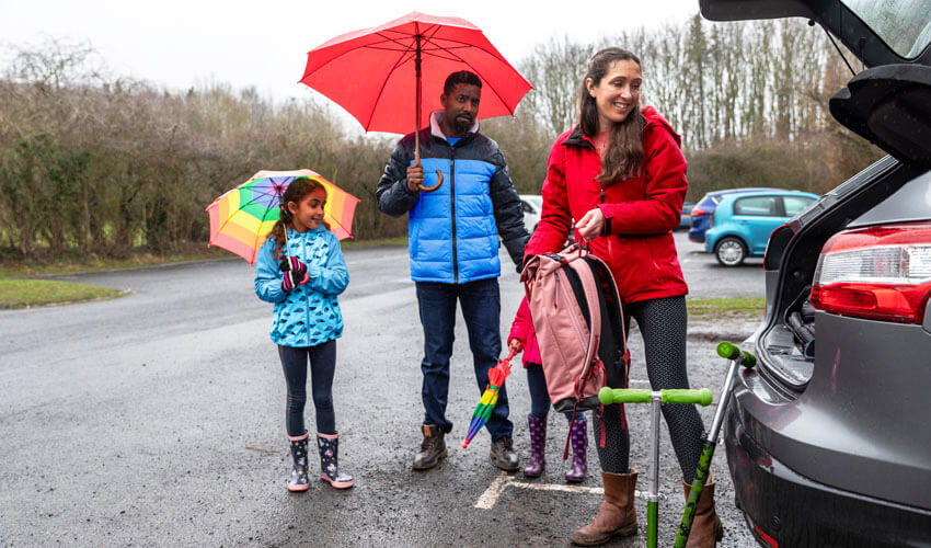 Family of three unloading scooter from SUV trunk in the rain