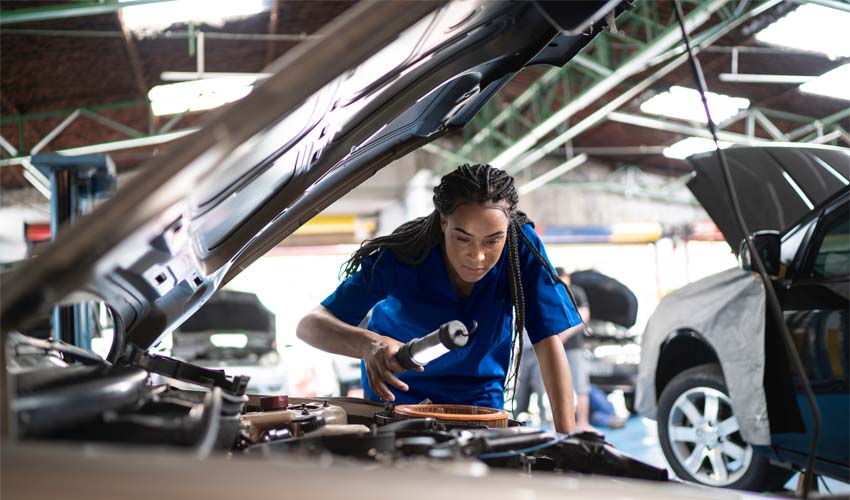 Female mechanic looking under hood of car in garage