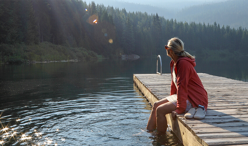Woman sitting on a dock dangling legs in the water.
