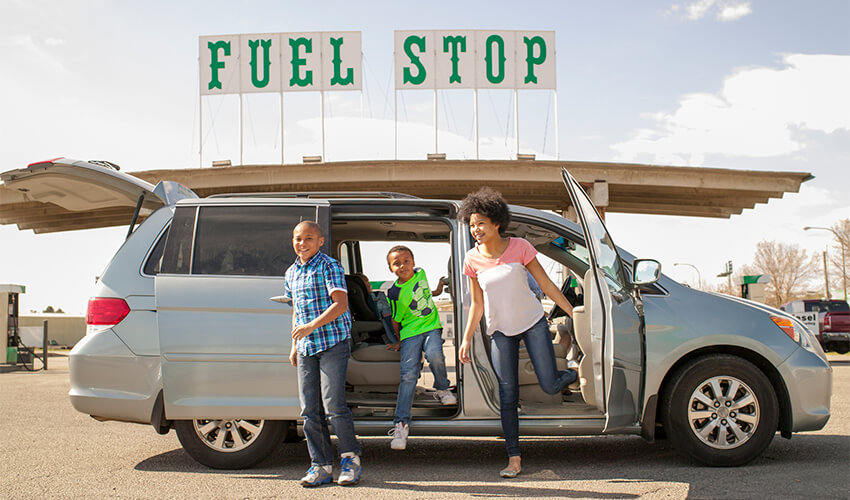 Two kids and mom excitingly exciting van at fuel stop.