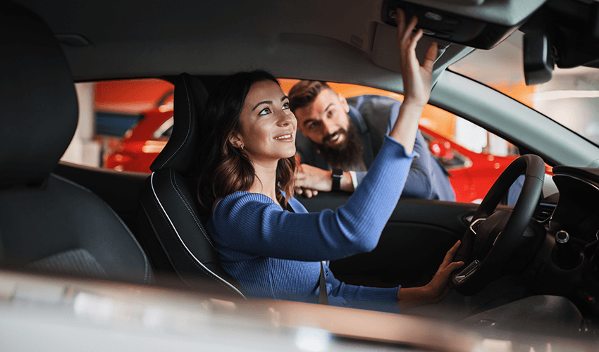 A woman sitting in a car checking car functions with a man looking along.