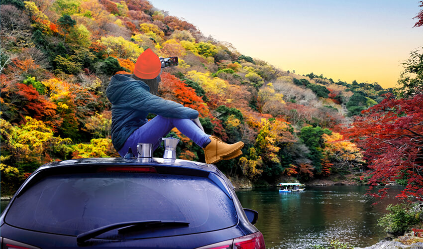 Woman on top of car admiring fall leaves.
