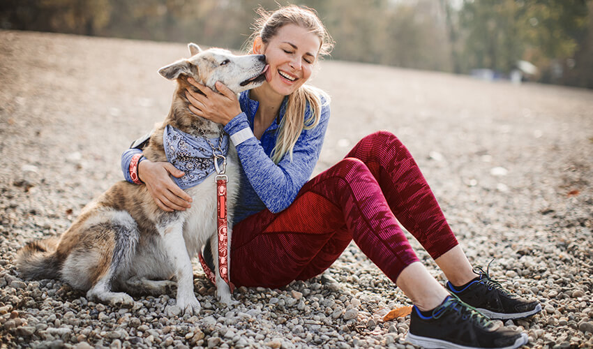 Smiling woman hugging her big dog on a beach.