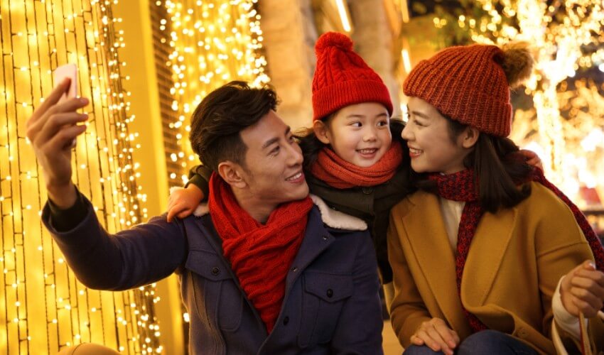 Parents taking a photo with their young daughter at an outdoor holiday event. 