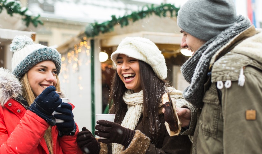 Three friends enjoying hot chocolate at a Christmas market.