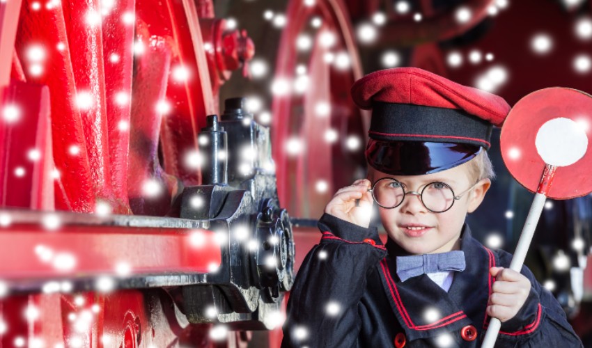 Young boy dressed as a train conductor standing beside a train.