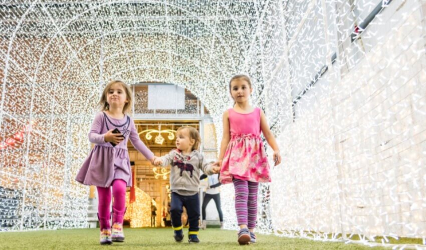 Three young children walking down an archway of lights at Glow Gardens festival of lights.