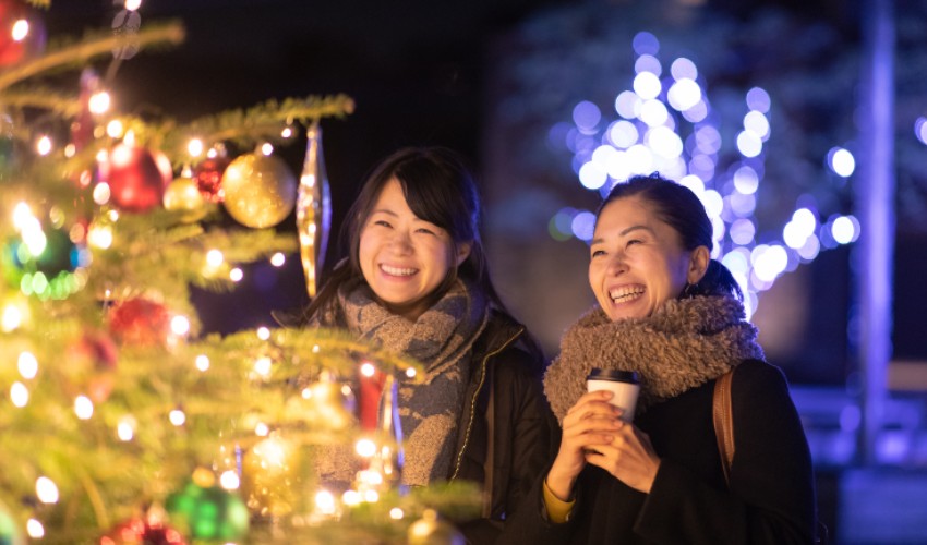 Two smiling female friends enjoying Christmas lights outdoors.