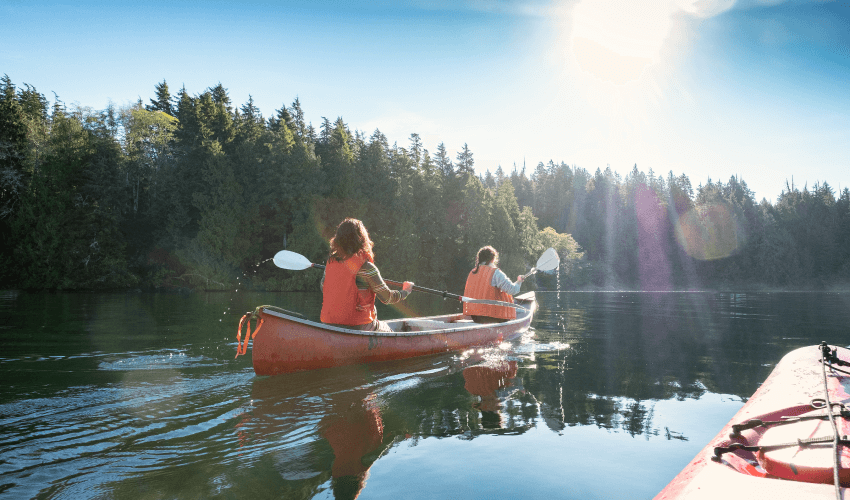 Two women canoeing on water surrounded by trees.