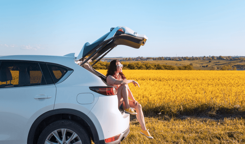 Smiling woman sitting in suv car trunk looking at sunset.