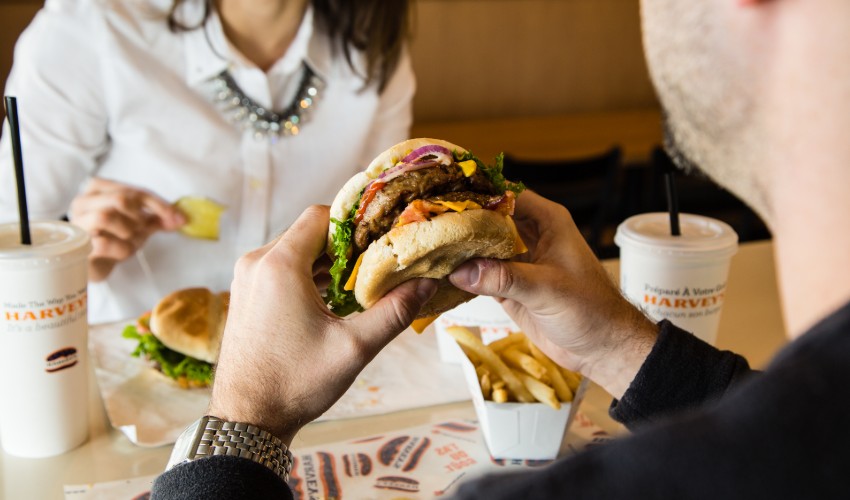Man holding harveys hambuger close to mouth.