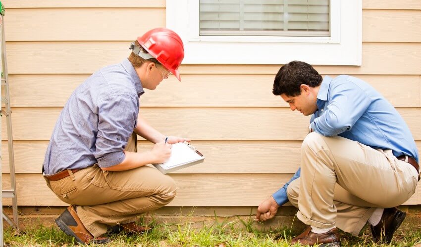 Home inspectors examining a home’s exterior wall and foundation.