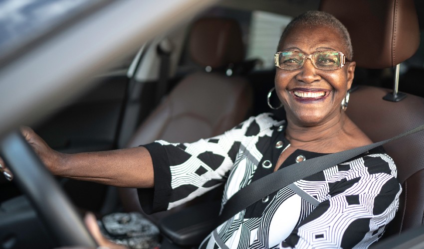 Happy senior citizen wearing a seat belt and sitting behind the wheel of a car.
