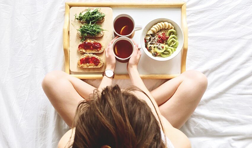 Overhead shot of woman having a healthy breakfast with tea in bed.
