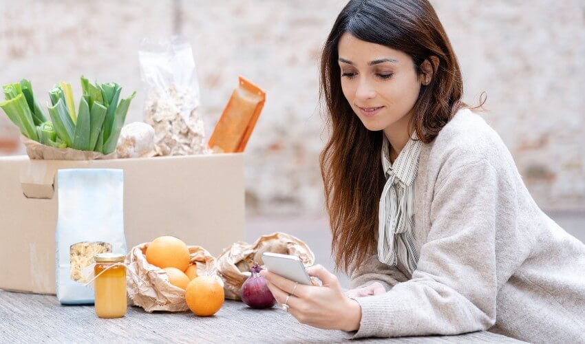 Woman checking her fresh vegetable delivery while holding her mobile phone.
