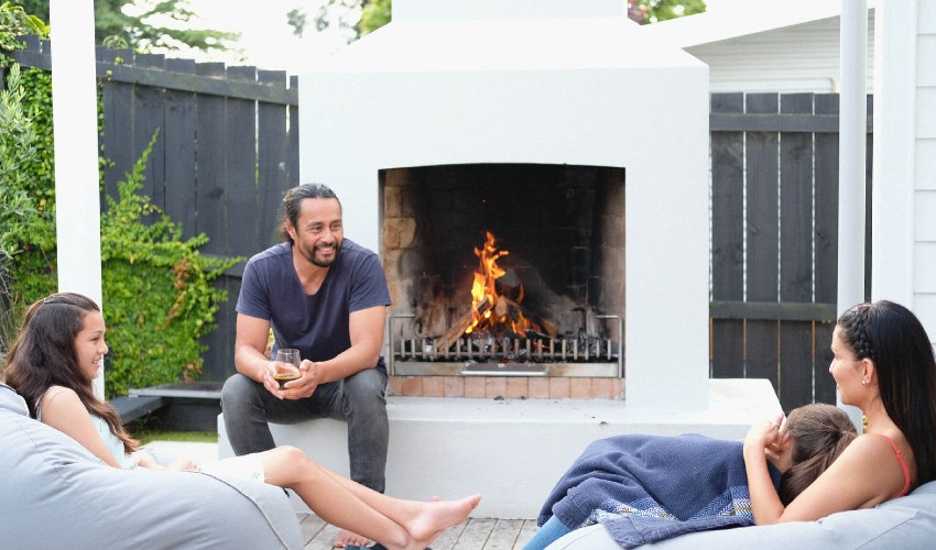 Family seated on backyard patio next to outdoor firelace.