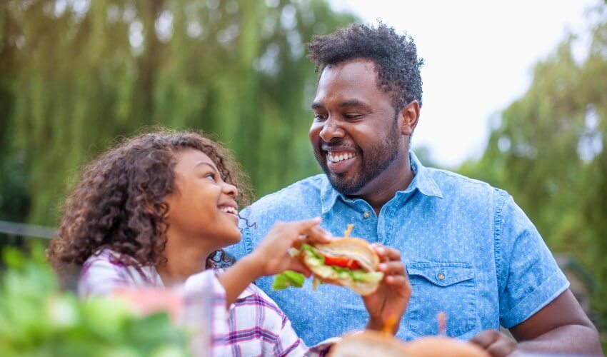 Father and daughter eating at a picnic.