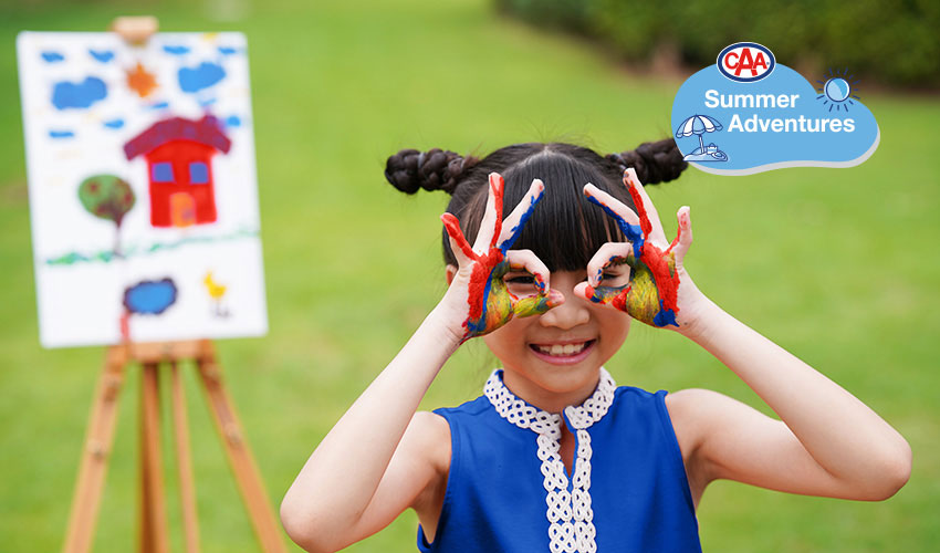 Young girl outdoors with artwork on easel hands covered in paint