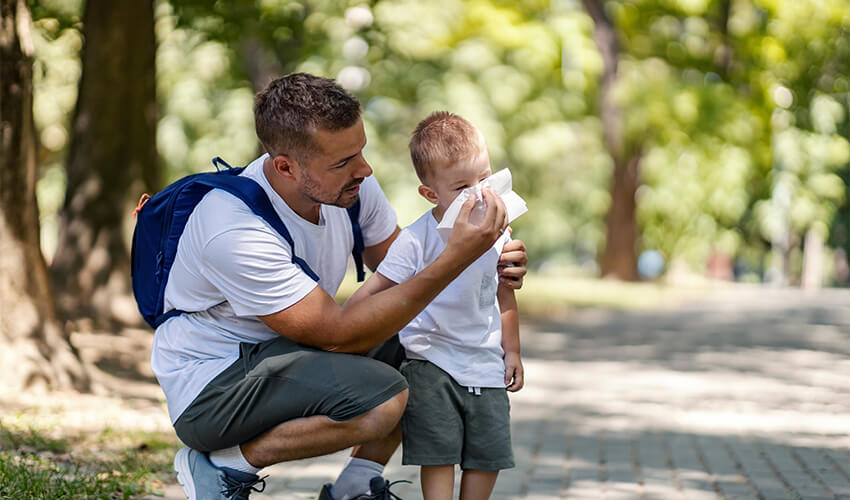 Dad helping his son blow his nose while outside.