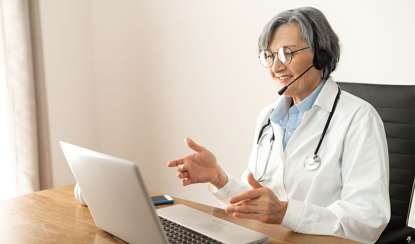 Senior doctor giving consultation to a patient online through laptop.