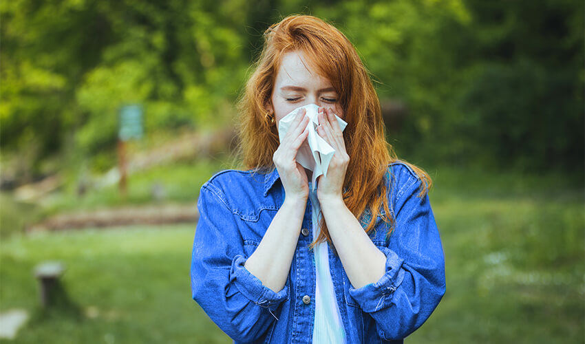 Young woman blowing her nose while outside in the spring.