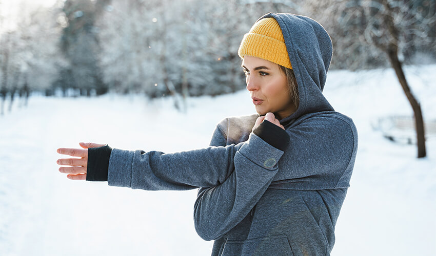 A woman is stretching in a winter surrounded by snow.