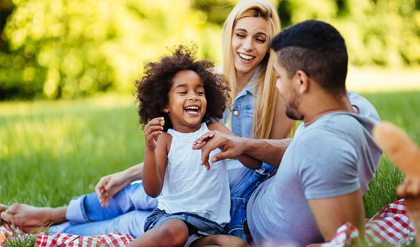 Parents with a child sitting on a blanket in a green field.