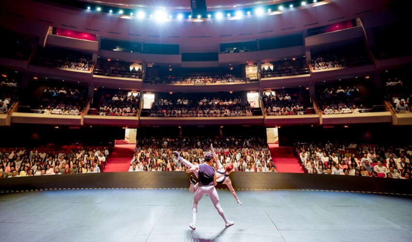 Ballet dancers performing on stage for a large public at a theater.