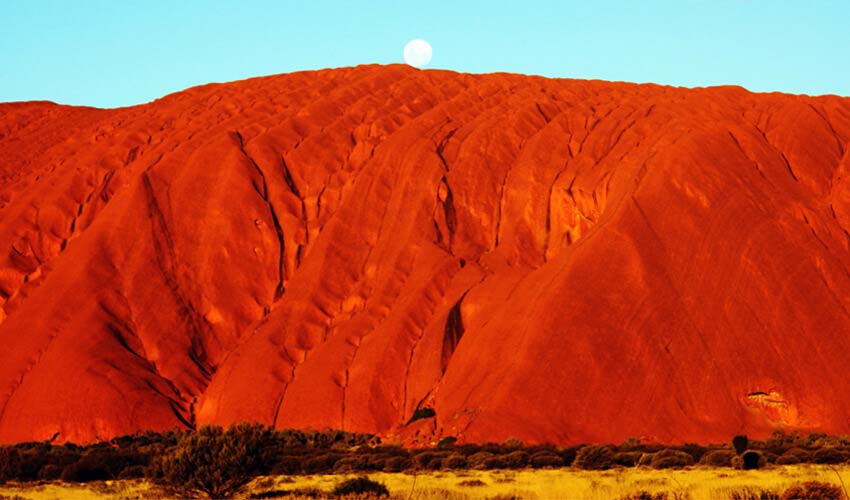 Brilliant red façade of Ayer’s Rock contrasting against bright blue sky.