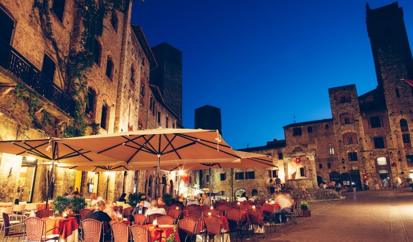 People dining outside on an Italian piazza at dusk.