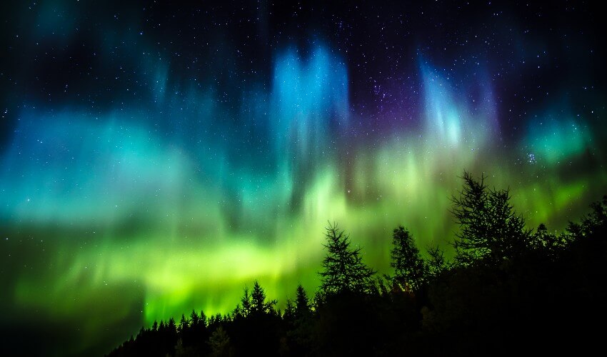 Star-filled night sky streaked with vibrant blues and greens of The Northern Lights.