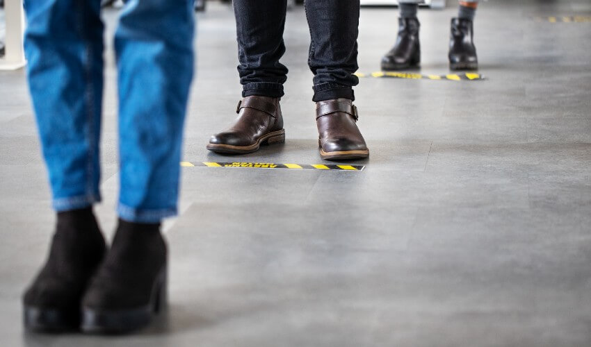Low angle showing people standing behind social distancing signage on the floor.