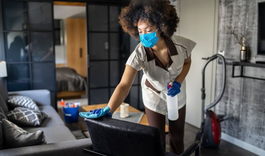 Maid wearing a non-medical mask cleaning a hotel room.