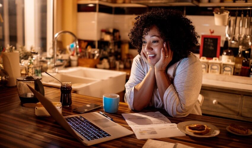 Enthralled woman watching movie on laptop at kitchen counter.