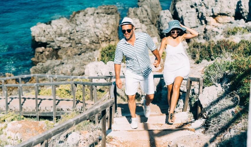 Young couple climbing stone stairs with Mediterranean in background.