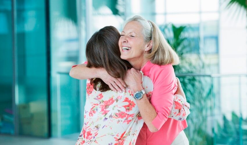 Adult daughter and mother hugging at airport.