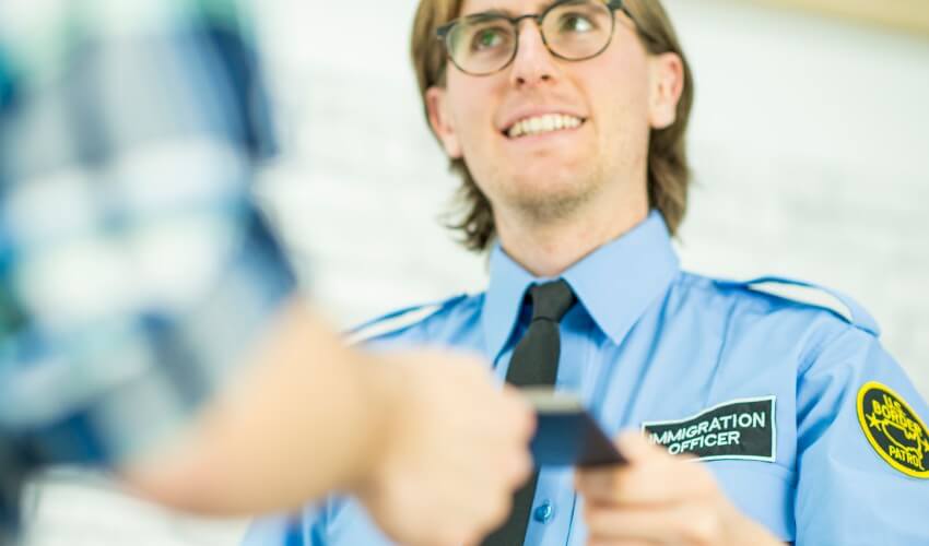 Smiling immigration officer taking passport from traveller.