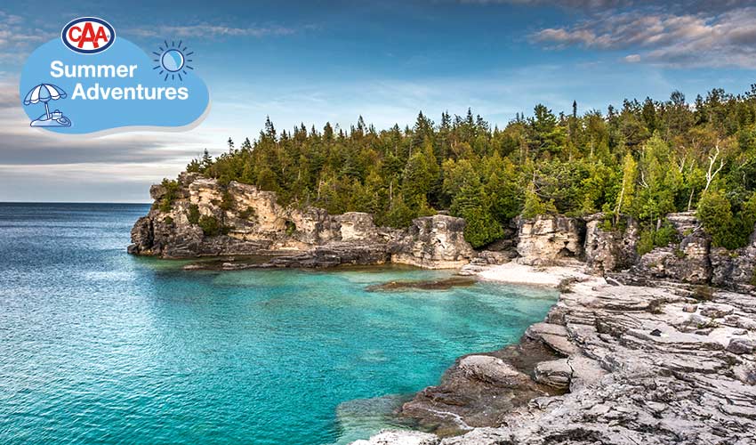 The shore of Lake Huron surrounded by evergreen trees and rocks.
