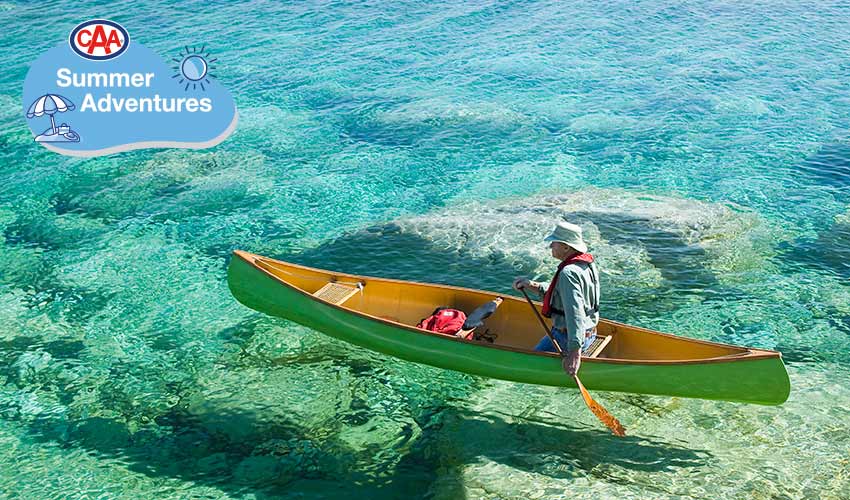 Man canoeing over shallow water and rocks.