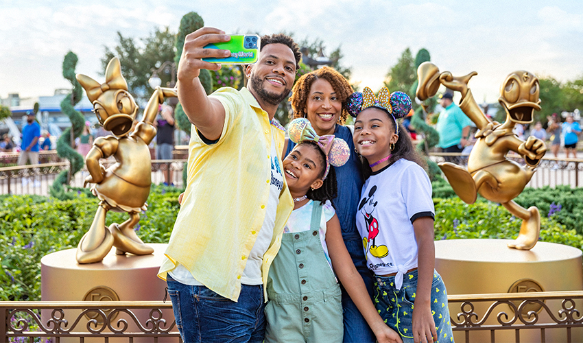 Happy family of four taking selfie at Disney. As to Disney artwork, logos and properties: ©Disney