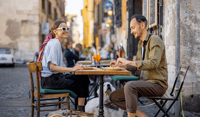 Man and woman eating italian pasta and drinking cocktails at restaurant on the street in Rome.