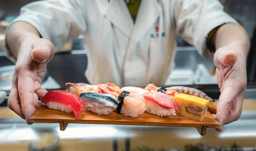 Male chef holding a wooden plate full of sushi.