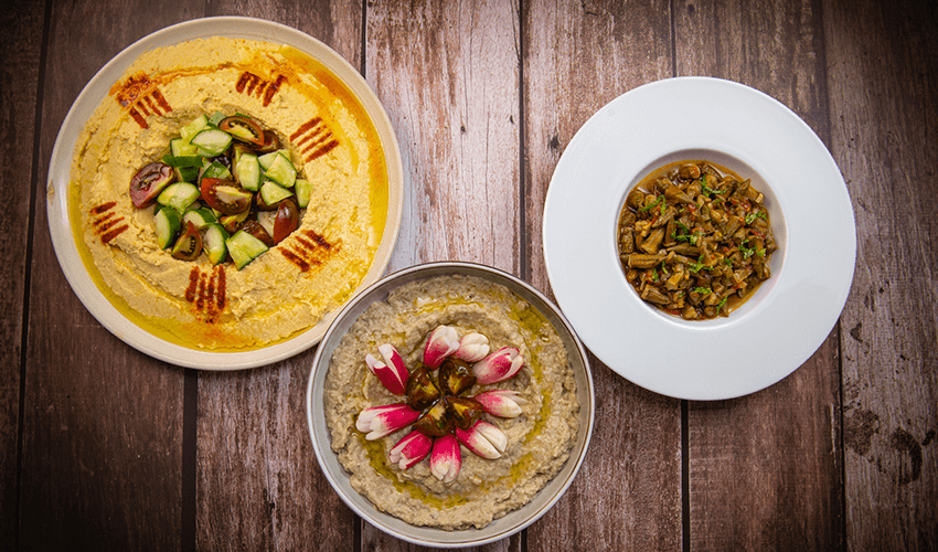A table with dishes: Lebanese meze, hummus, aubergine caviar and okra in tomato sauce.