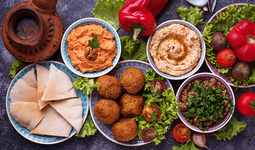 A table filled with selection of Middle eastern or Arabic dishes like Falafel, hummus, pita, muhammara and other.
